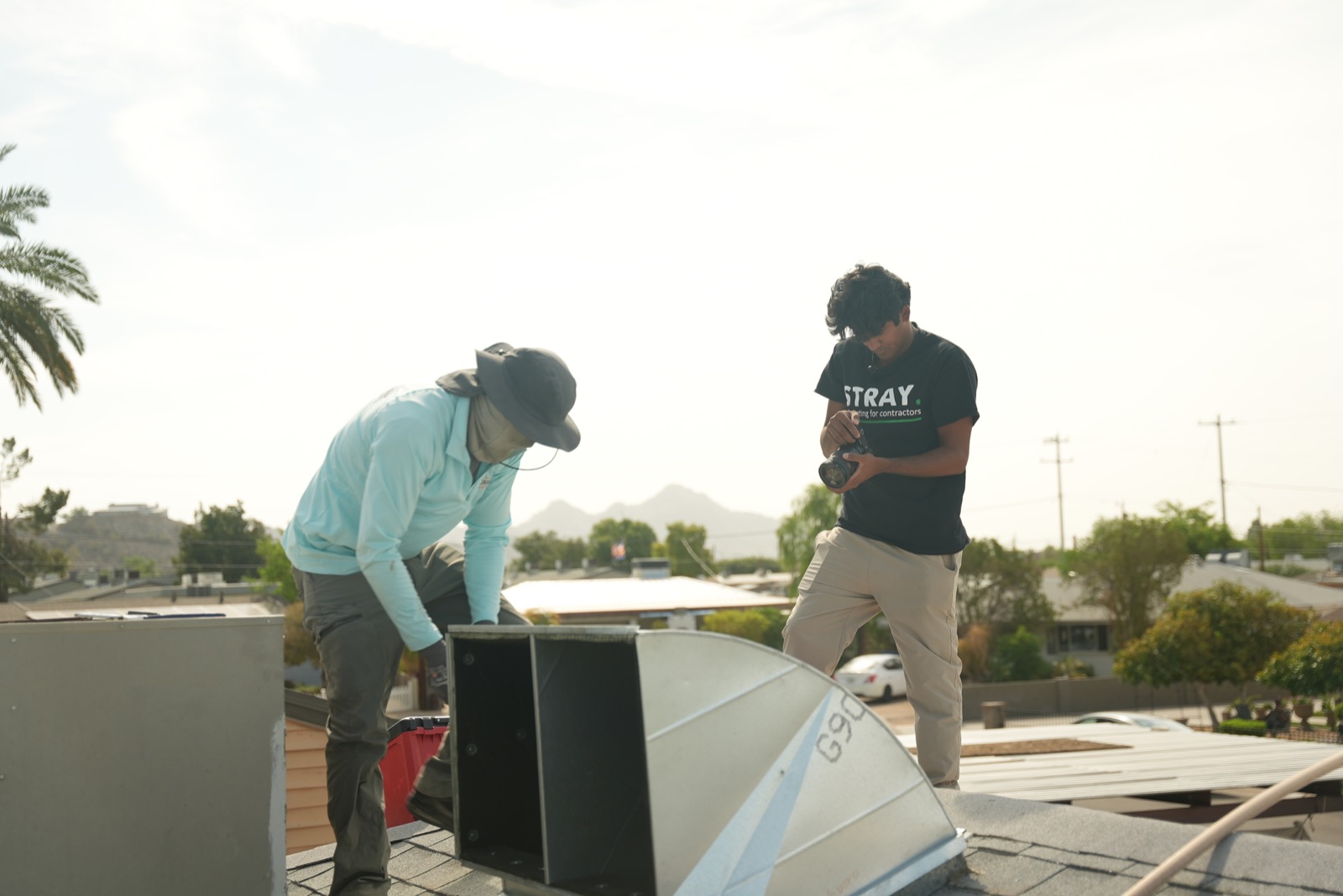 A Stray videographer reviewing footage with a contractor beside rooftop HVAC equipment in Arizona